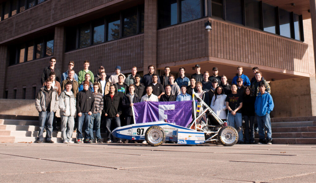 a bunch of engineering students standing around a race car