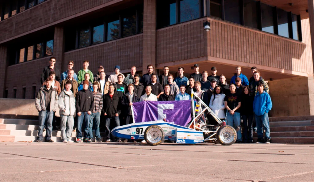 a bunch of engineering students standing around a race car